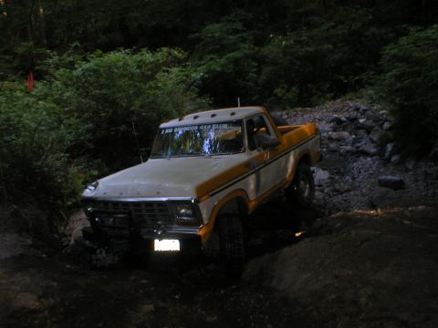 1978 Ford Bronco - A 1978 Ford Bronco navigates a challenging, rocky off-road path surrounded by dense foliage.