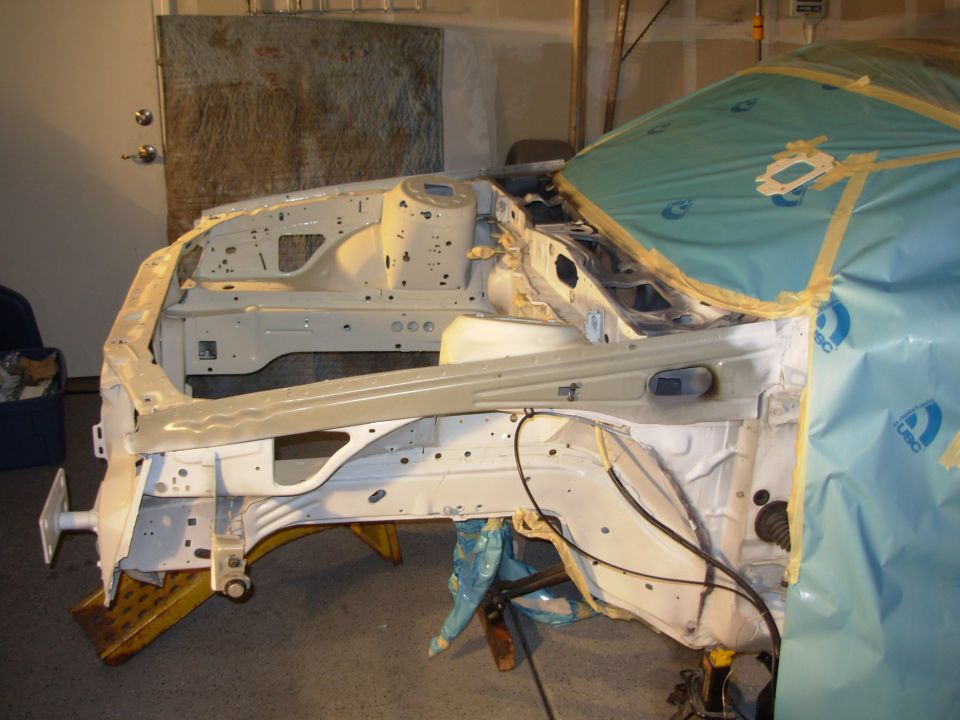 Car frame stripped down, covered in protective sheeting, undergoing restoration