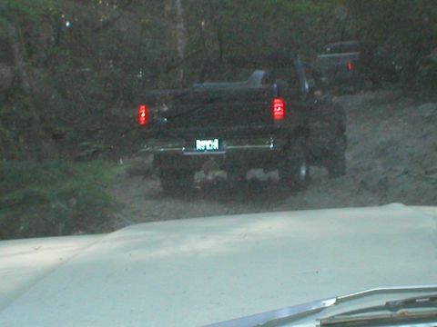 1978 Ford Bronco - A black SUV navigates a muddy, wooded trail, with a second vehicle visible in the distance.