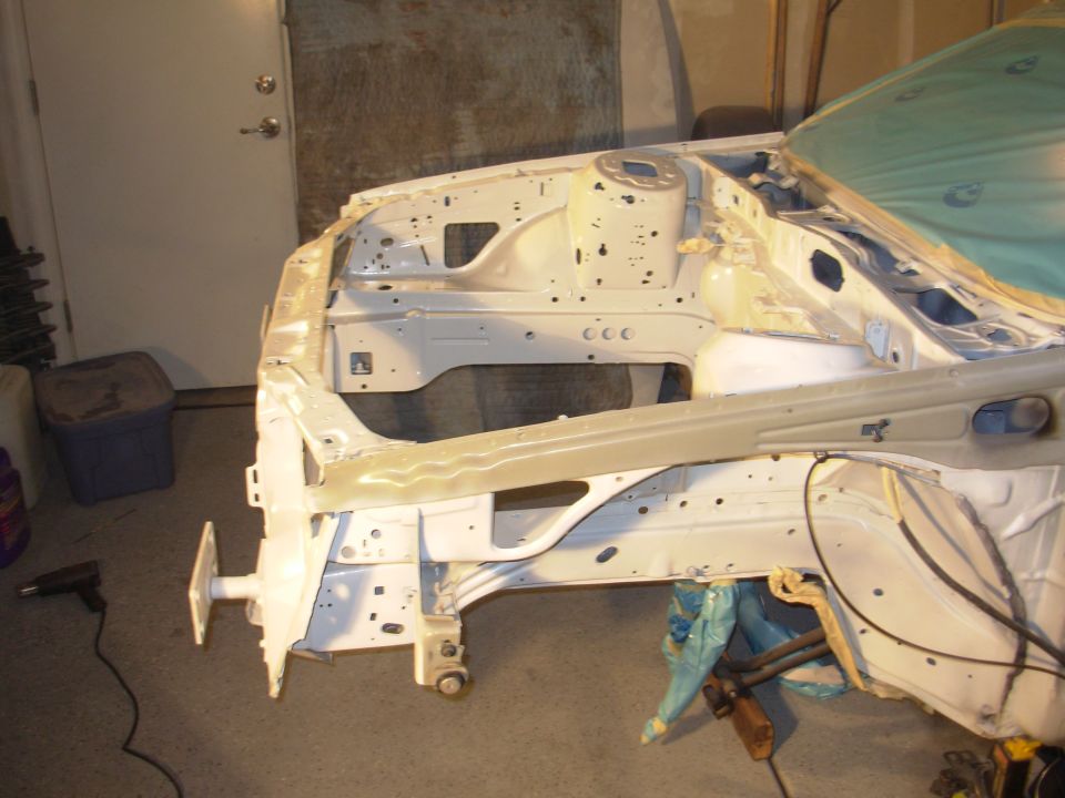Car frame stripped down, showing suspension mounts and inner fender structure