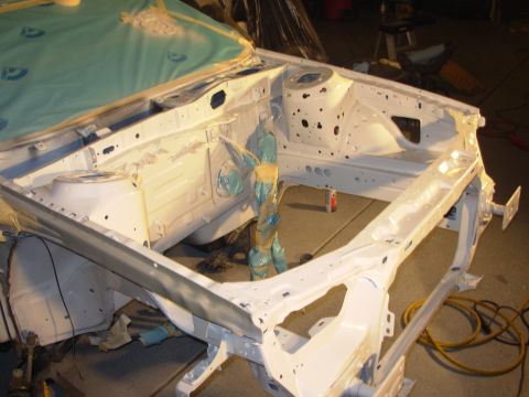 1991 Ford Taurus - The bare frame of a car is being prepared for painting, with the engine bay area covered and protected.