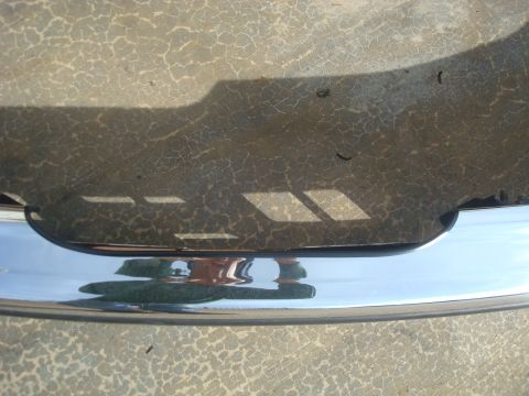 1995 Ford Bronco - A close-up of a chrome bumper against a textured concrete surface, with a website logo in the corner.