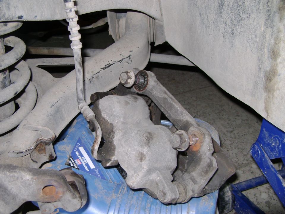 Close-up of a car's brake caliper and suspension linkage, with a blue drip pan underneath