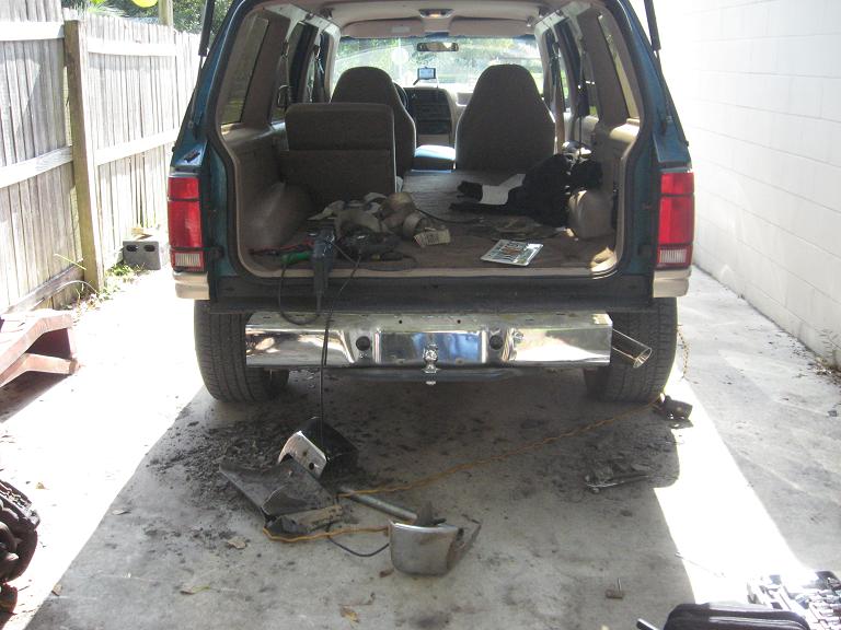 Rear view of a 1995 Ford Explorer with the tailgate open, showing the interior cargo area and a removed bumper on the ground