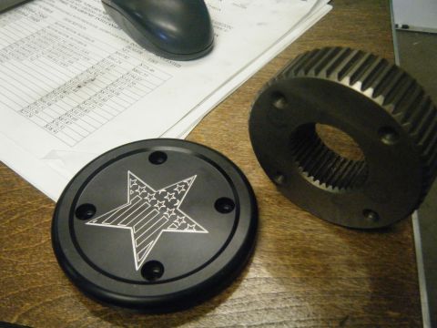 1978 Ford Bronco - A black hubcap an American flag star design sits next to a metal gear on a wooden surface with papers and a computer mouse.