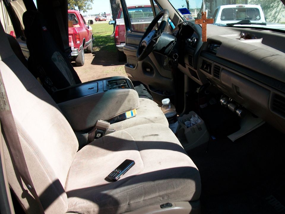 Interior of a 1996 Ford F-250, showing the passenger seat, dashboard, and center console. Other trucks are visible outside