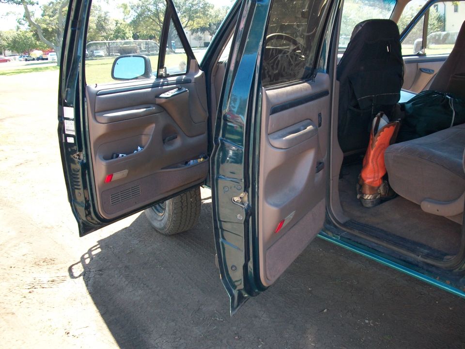 Green truck interior with doors open, showing brown door panels, a steering wheel, and a pair of orange boots on the passenger seat