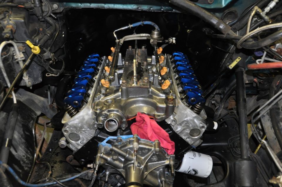 Close-up of a V8 engine with shiny metal parts and bright blue valve covers. A red rag is stuffed into the engine
