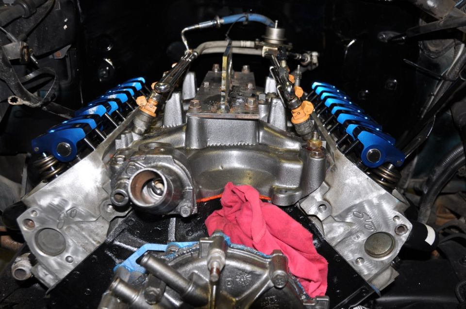 Engine block with blue roller rockers, fuel injectors, and a red rag. Close-up view