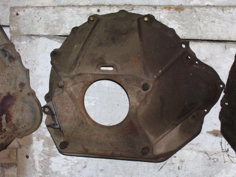 Rusty cast-metal bellhousing with central bore and mounting bolts on white wood planks