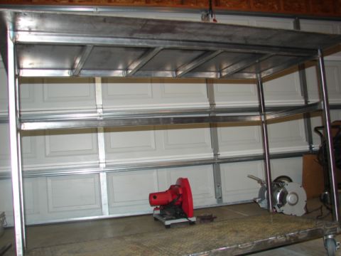 1996 Ford Bronco - A metal shelving unit stands in a garage, with a red chop saw and a grinder visible on the floor.