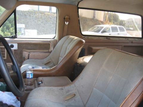 1986 Ford Bronco - The interior of an older SUV shows custom bucket seats and a spare tire. A white SUV is seen through the rear window.
