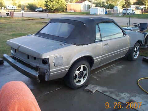 1984 Ford Mustang - A convertible car is parked outside, appearing to be in a state of repair or disassembly.