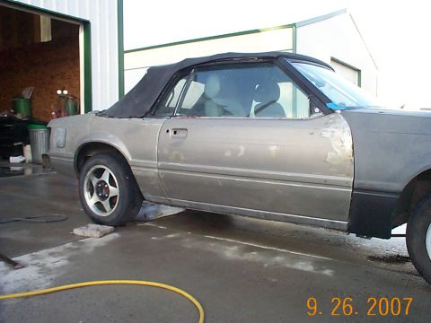 1984 Ford Mustang - A gray convertible car sits in a garage, showing signs of body damage and repair work.