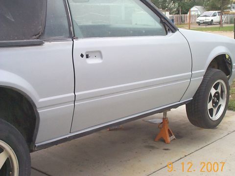 1984 Ford Mustang - A silver 1984 Ford Mustang convertible is shown on jack stands, with its side profile visible.