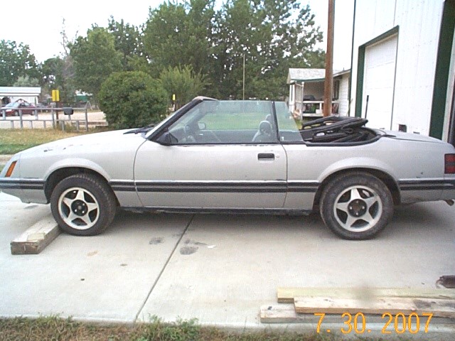 Silver convertible with black top folded down, side view, parked on concrete
