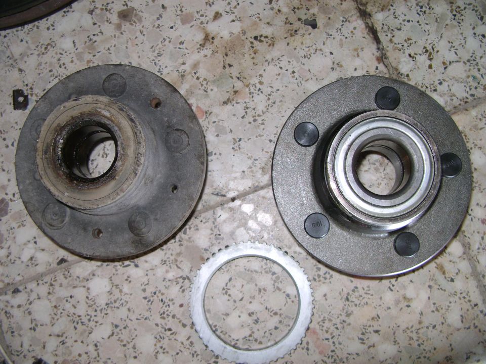 Two wheel hub assemblies and a toothed ring on a speckled surface. One hub is used, the other is new with a bearing