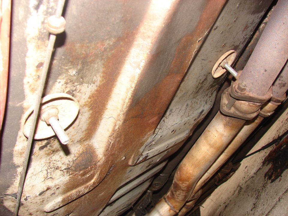 Rusty underbody floor pan with threaded studs and clamped exhaust pipe