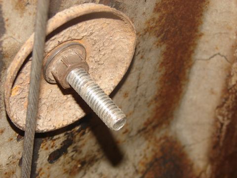 1973 Ford Ranchero - A close-up view of a bolt and washer assembly on a heavily rusted metal surface, with a cable present.