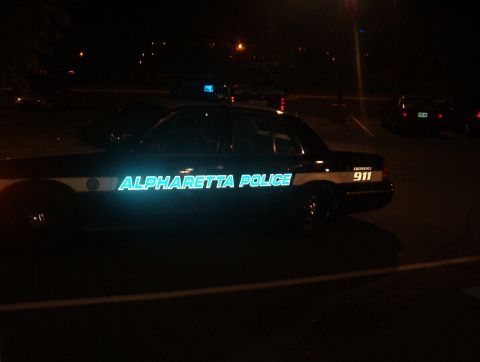1998 Ford Taurus - A police car with 'ALPHARETTA POLICE' written on its side is parked at night.