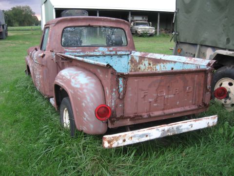 1966 Ford F-250 - This weathered Ford pickup truck, likely from the mid-1950s, sits in a grassy area next to a building.