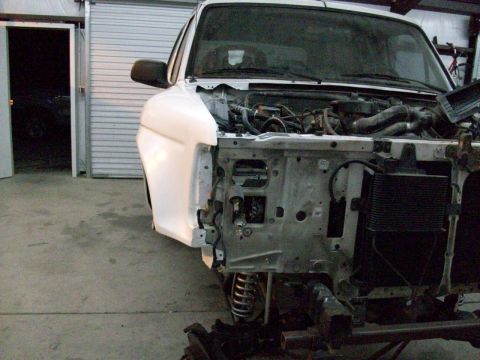 1996 Ford Bronco - A white truck is partially disassembled in a garage, revealing its engine and chassis.