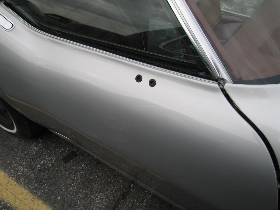 Silver car door with two black circular trim pieces near window