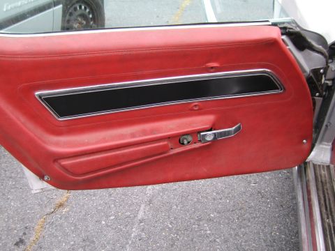 1991 Ford LTD Crown Victoria - Close-up of a red car door panel a chrome handle and black accent trim.
