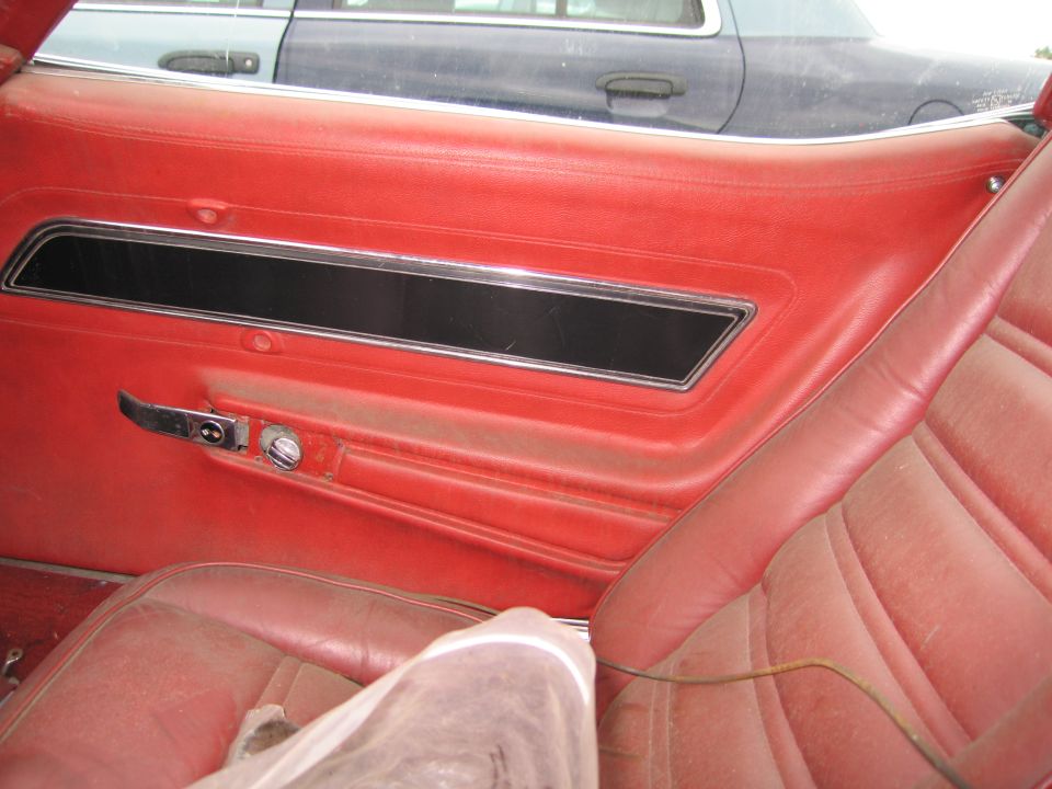 Red interior door panel and seat with chrome accents. Another vehicle is visible through the window