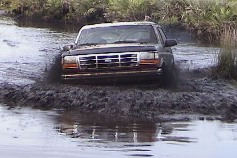 1993 Ford Bronco - A Ford truck navigates a muddy trail, kicking up water and mud.