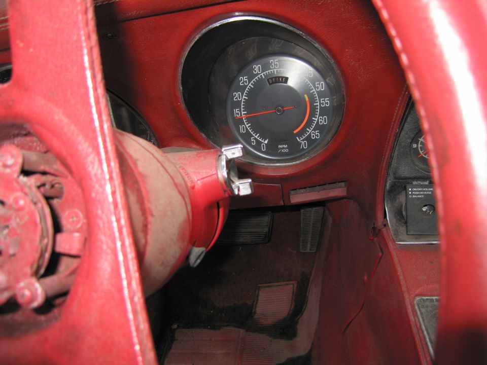 Red car interior with a dusty dashboard and steering wheel, showing a speedometer and brake warning light
