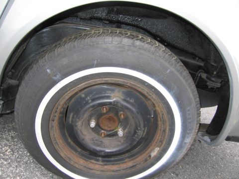 1991 Ford LTD Crown Victoria - A close-up view of a whitewall tire and a rusty steel wheel within the wheel well of a vehicle.