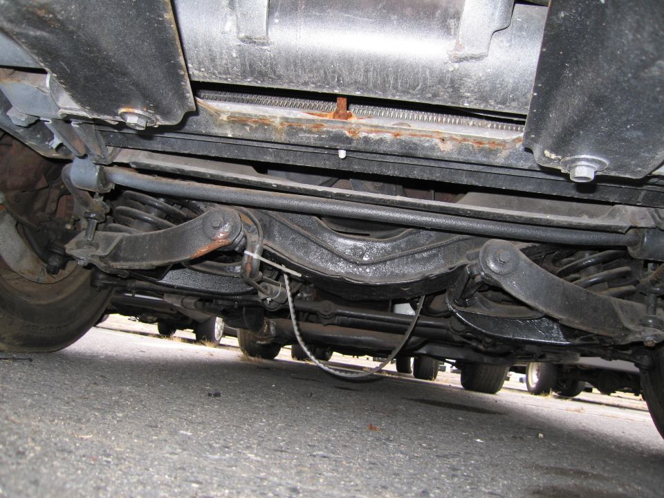 Undercarriage view showing suspension components and exhaust system. Multiple vehicles visible in the background