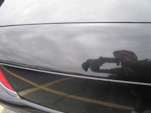 1991 Ford LTD Crown Victoria - Reflection of a photographer on the black trunk of a car, with yellow parking lot lines visible below.