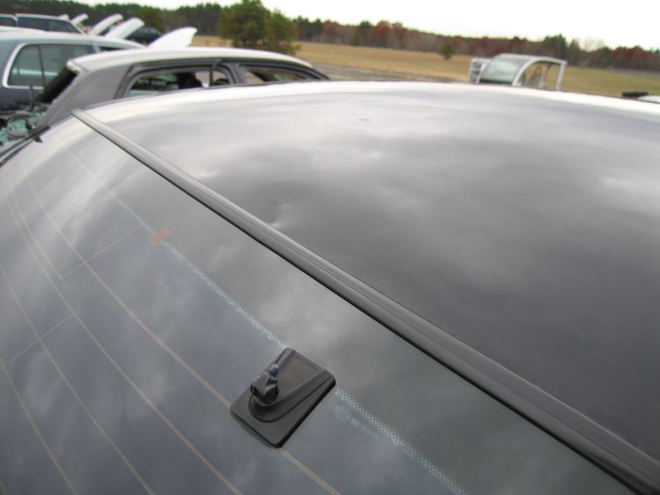 Rear window with antenna base on a dark car, other vehicles in background