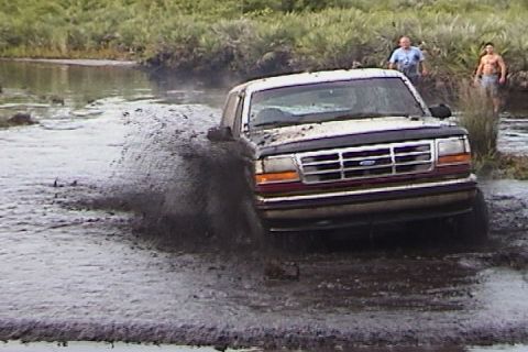 1993 Ford Bronco - A 1993 Ford Bronco navigates a muddy waterway, kicking up a large spray.