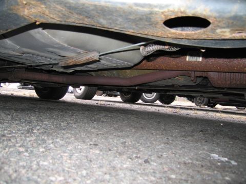 1991 Ford LTD Crown Victoria - The underside of a car reveals significant rust and a portion of the exhaust system, with other vehicles visible in the background.