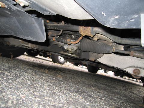 1991 Ford LTD Crown Victoria - A view of the steering and suspension system from underneath a vehicle, with other cars parked nearby.