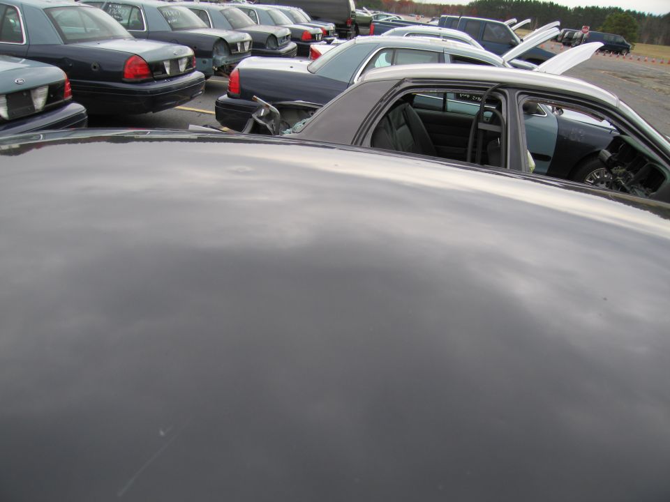Dark sedan interior with open doors, showing seats and dashboard. Multiple similar vehicles parked in background