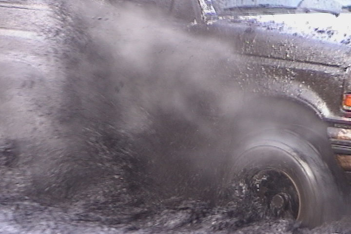 Truck rear tire spinning through a mud pit throwing a wall of muddy water