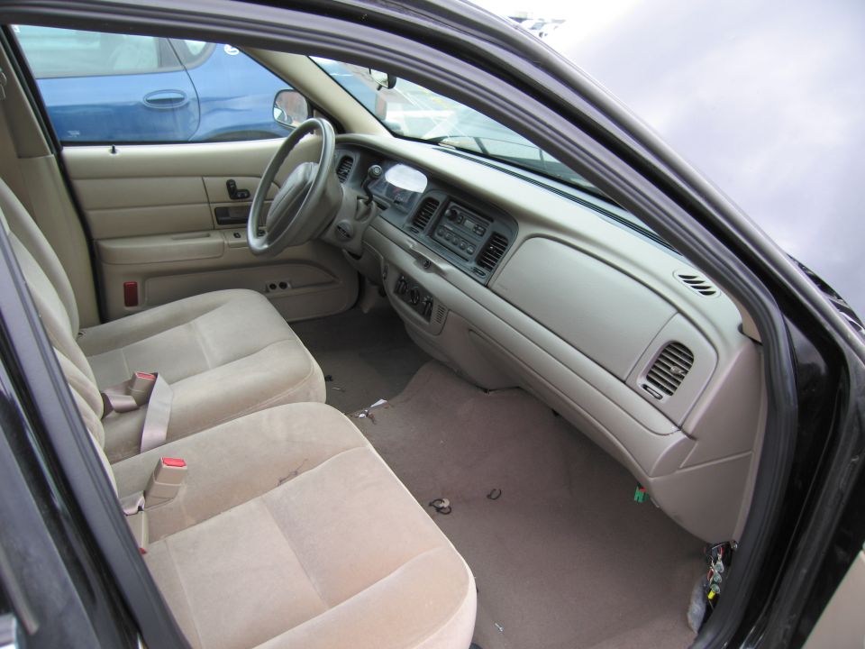 Interior of a black car showing tan seats, dashboard, and steering wheel. Another blue car is visible through the window