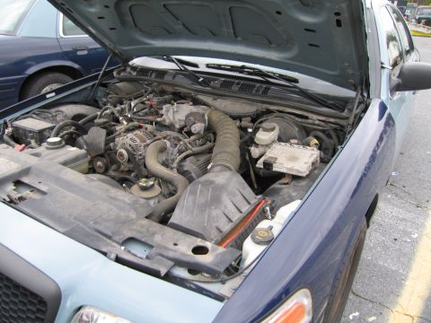 1991 Ford LTD Crown Victoria - Engine bay of a blue Ford Crown Victoria, with another similar vehicle parked nearby.