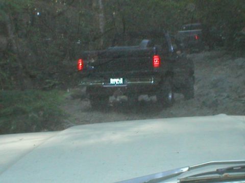 1993 Ford Bronco - A black pickup truck navigates a muddy off-road trail, with another vehicle following closely behind.