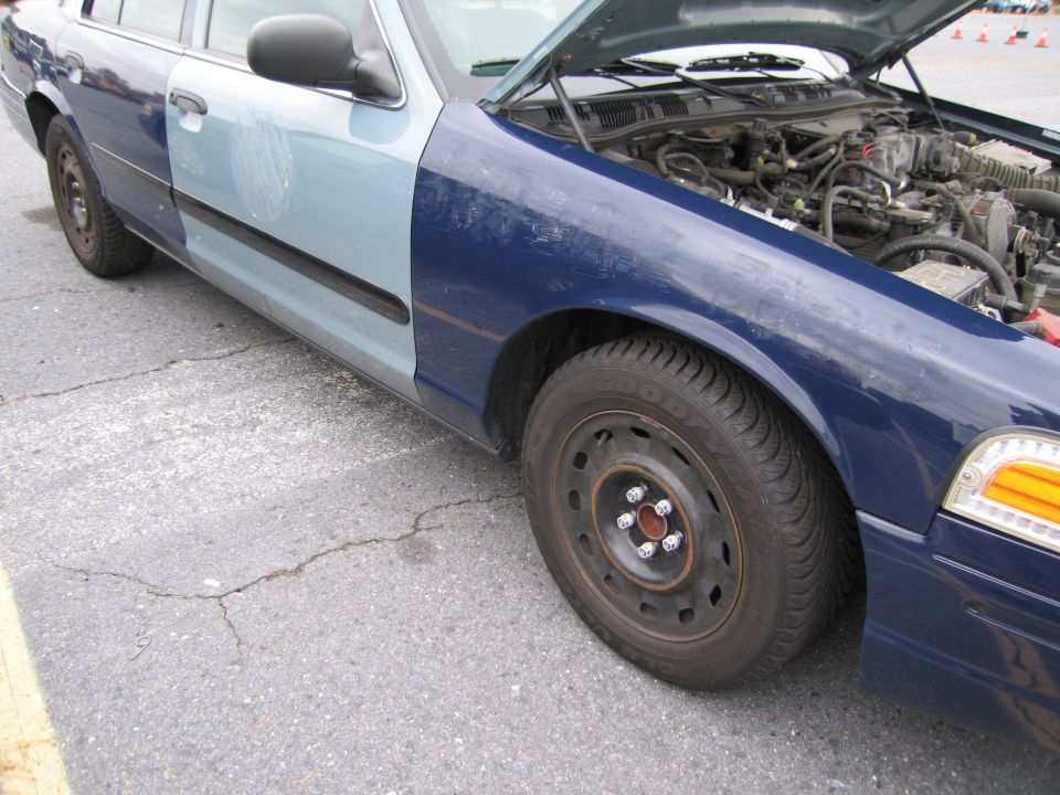 Blue Ford Crown Victoria with mismatched front fender and hood open, showing engine