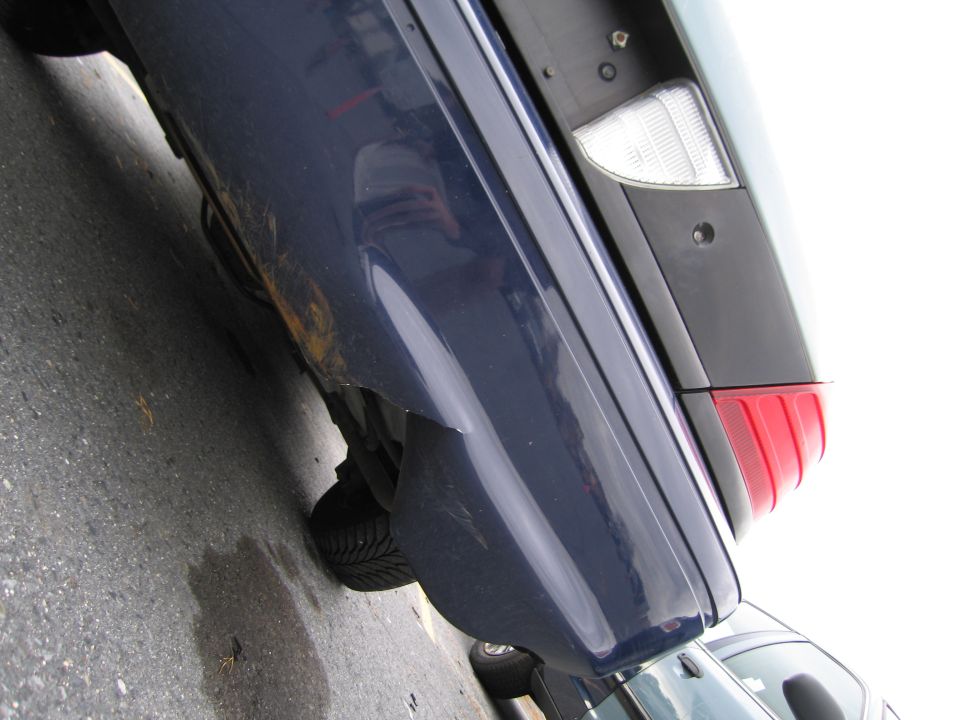 Blue car's rear quarter panel and taillight, showing rust and damage