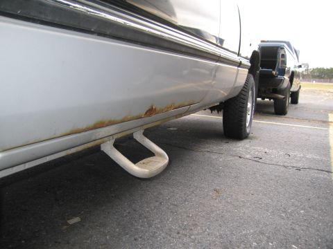 1991 Ford LTD Crown Victoria - Silver truck with running boards and visible rust on the lower panel, parked outdoors.