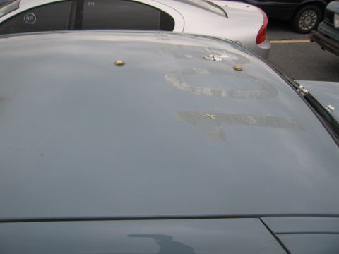 1991 Ford LTD Crown Victoria - The roof of a car shows faded numbers and two gold studs, with other vehicles visible in the background.