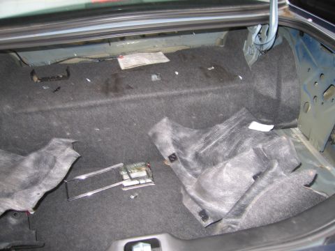 1991 Ford LTD Crown Victoria - The trunk of a car is shown with the carpet lining removed, revealing the underlying structure and some electrical components.