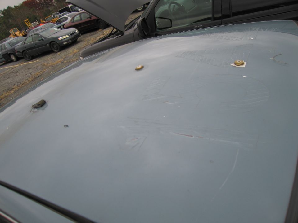 Gray car roof with three circular mounts and scratches. Other cars and yellow construction equipment in background