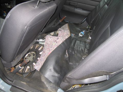 1991 Ford LTD Crown Victoria - The interior of a vehicle reveals exposed insulation and a spare tire beneath the rear seats, with a water bottle on the floor.